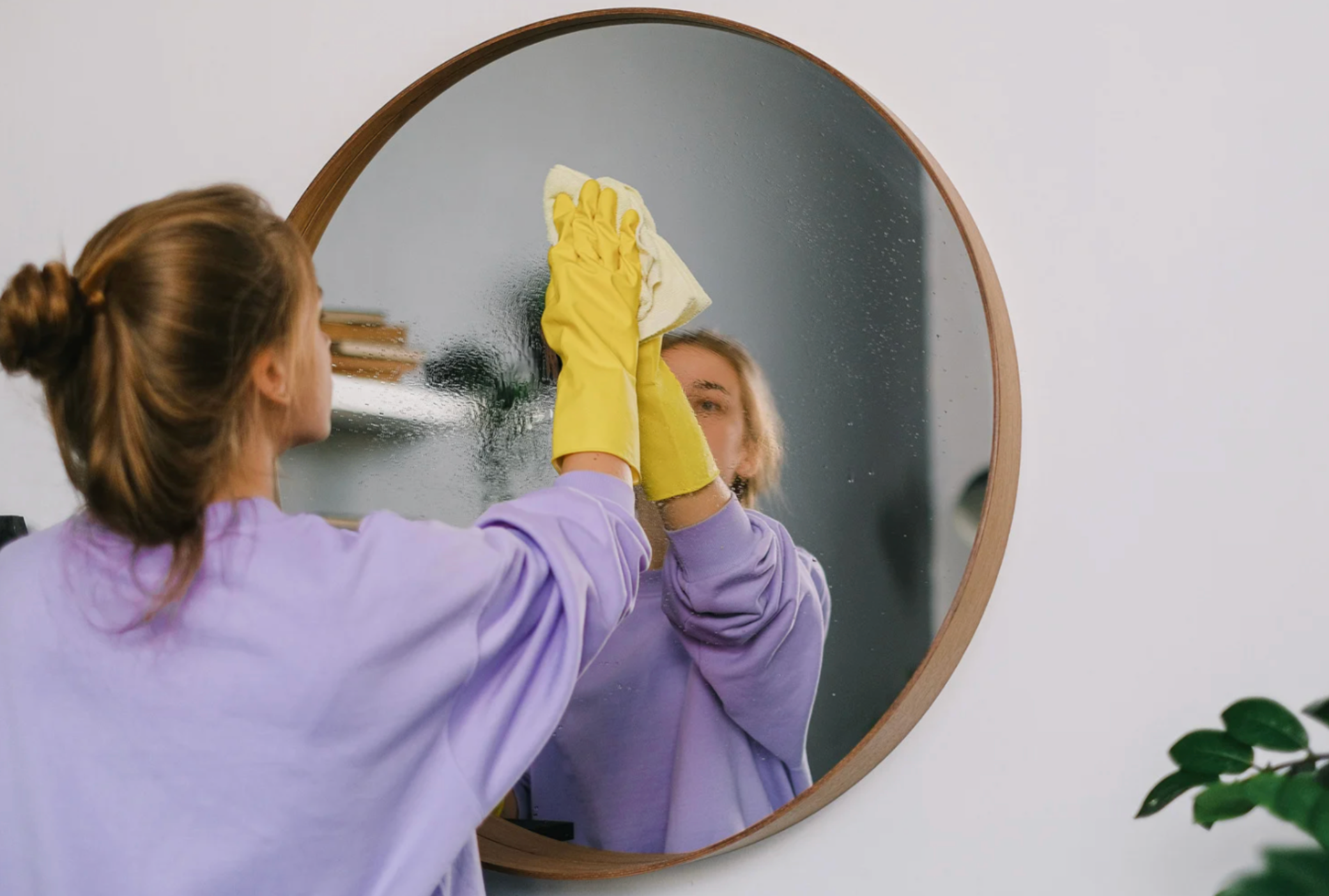 woman cleaning round mirror using natural cleaning products